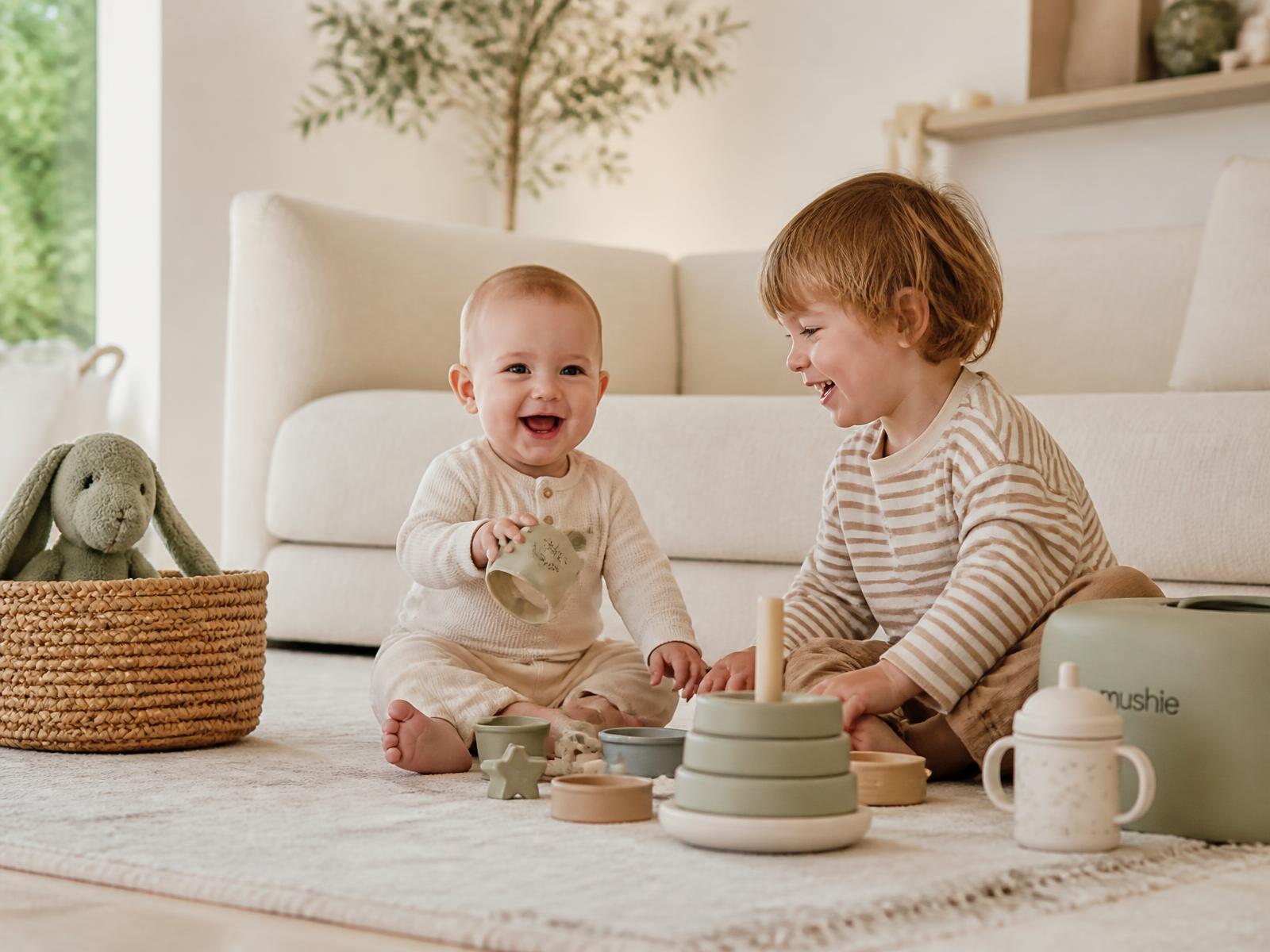 Two young children playing with soft baby products in a bright living room